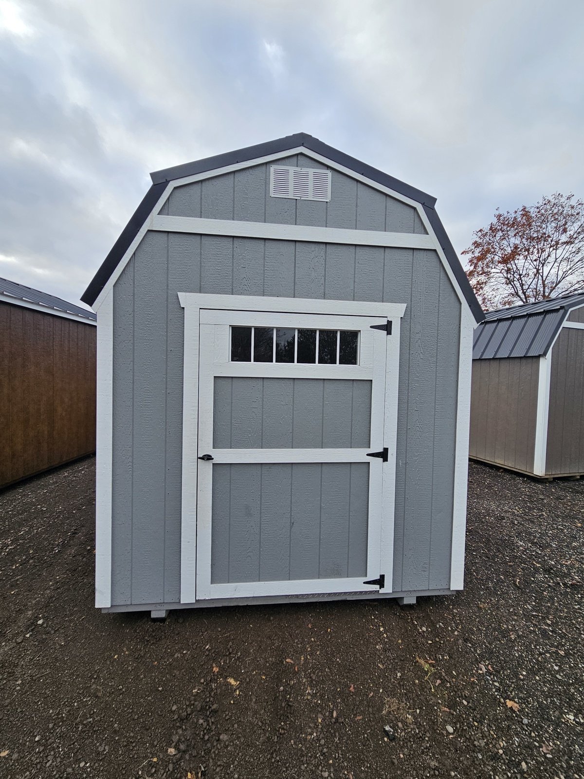 Gray gambrel shed with white trim and a windowed door